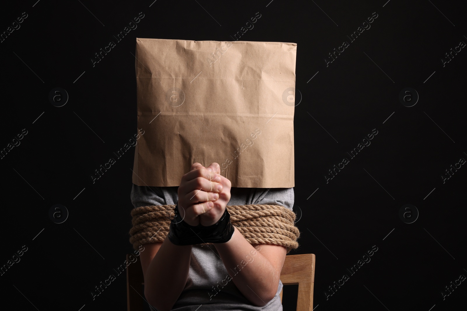 Photo of Little boy in paper bag tied up and taken hostage on dark background