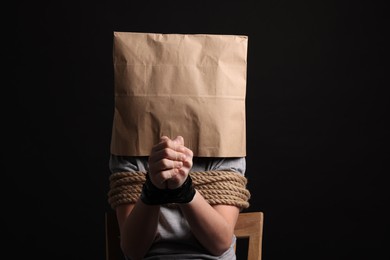 Little boy in paper bag tied up and taken hostage on dark background