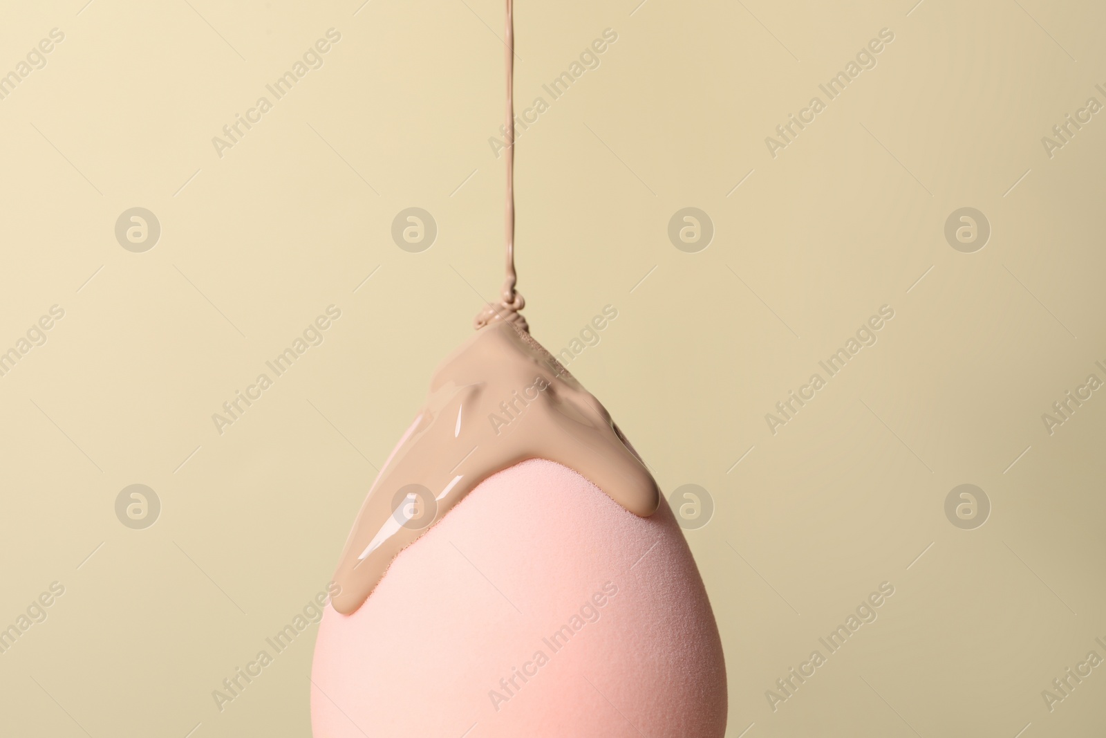 Photo of Skin foundation pouring onto makeup sponge on beige background