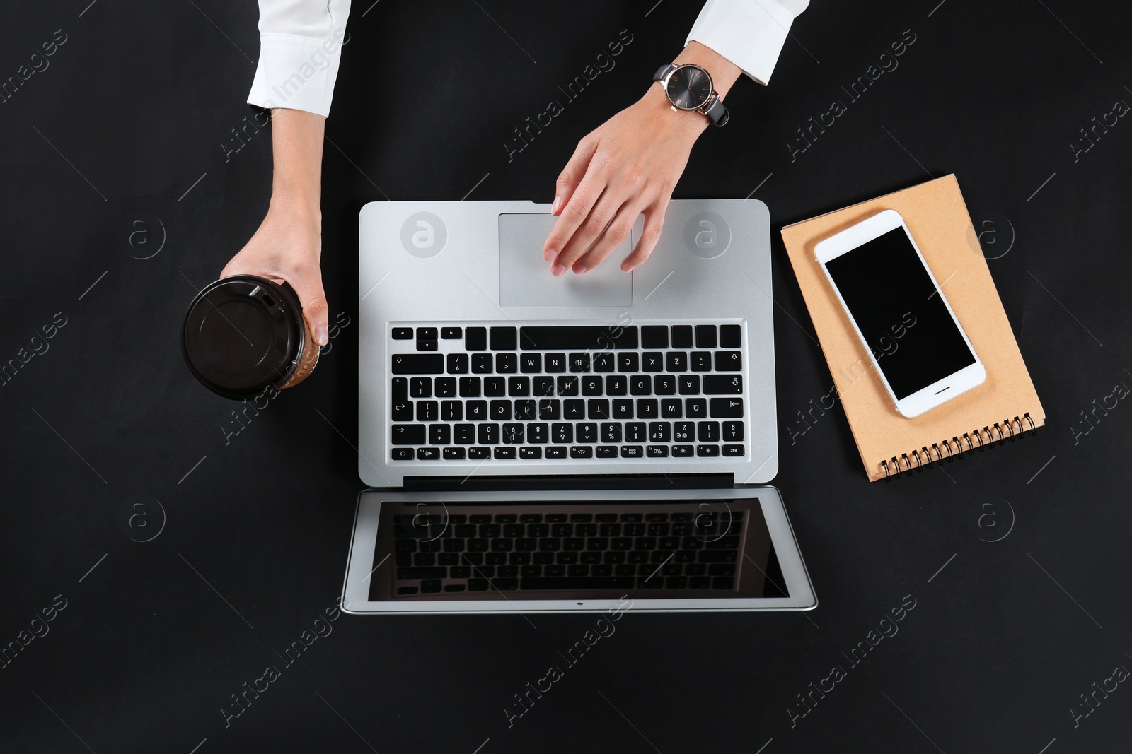 Photo of Young woman holding coffee while using laptop on black background, top view