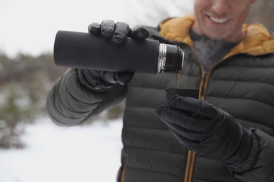 Photo of Man pouring hot drink from thermos into cap outdoors on snow day, closeup