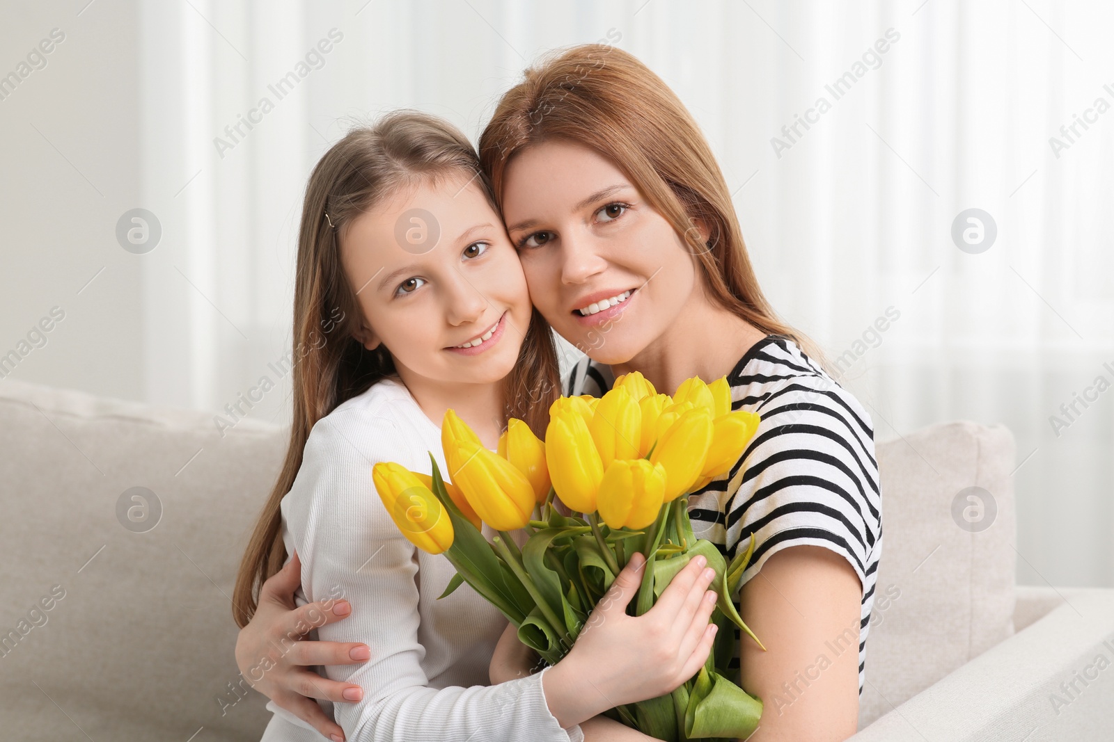 Photo of Happy mother and her cute daughter with bouquet of yellow tulips on sofa at home