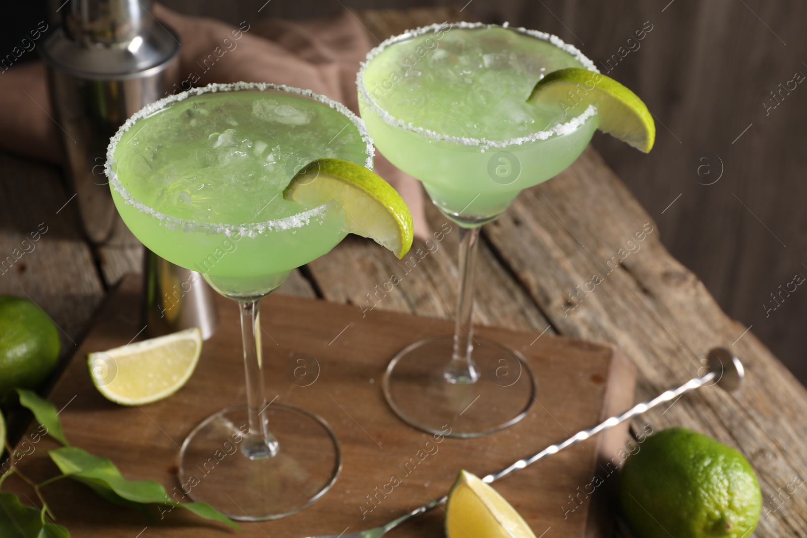 Photo of Delicious Margarita cocktail in glasses, limes and green leaves on wooden table