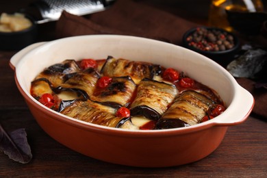 Tasty eggplant rolls with tomatoes and cheese in baking dish on wooden table, closeup