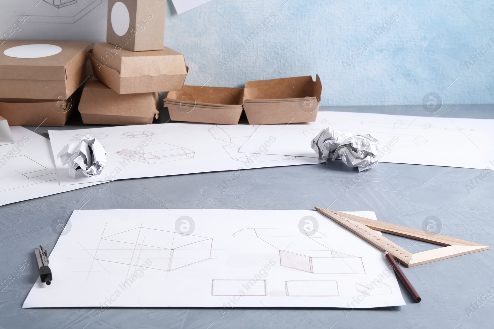 Photo of Creating packaging design. Drawings, boxes and stationery on blue textured table, closeup