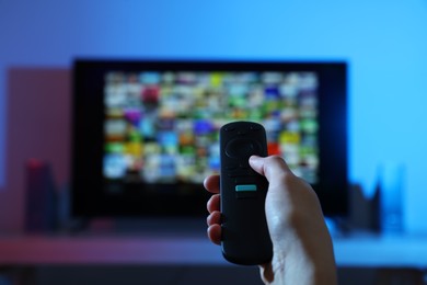 Photo of Woman switching channels on TV set with remote control at home, closeup