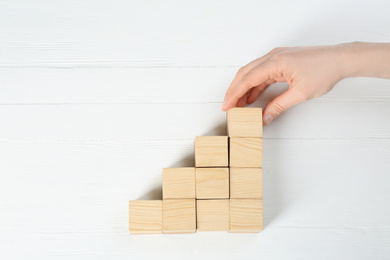 Woman building stairs with cubes on white wooden background, top view. Career promotion concept