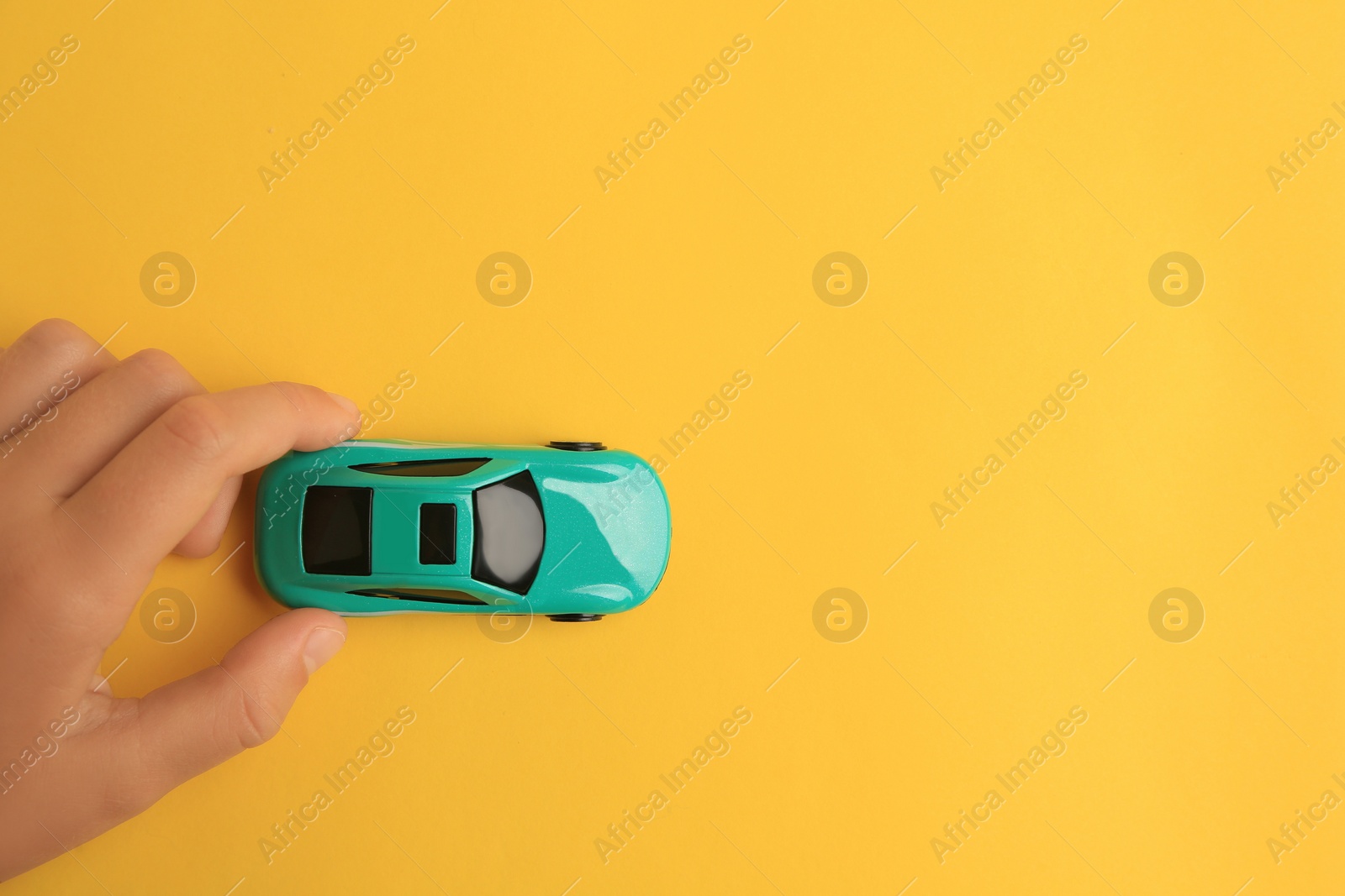 Photo of Child playing with toy car on yellow background, top view. Space for text