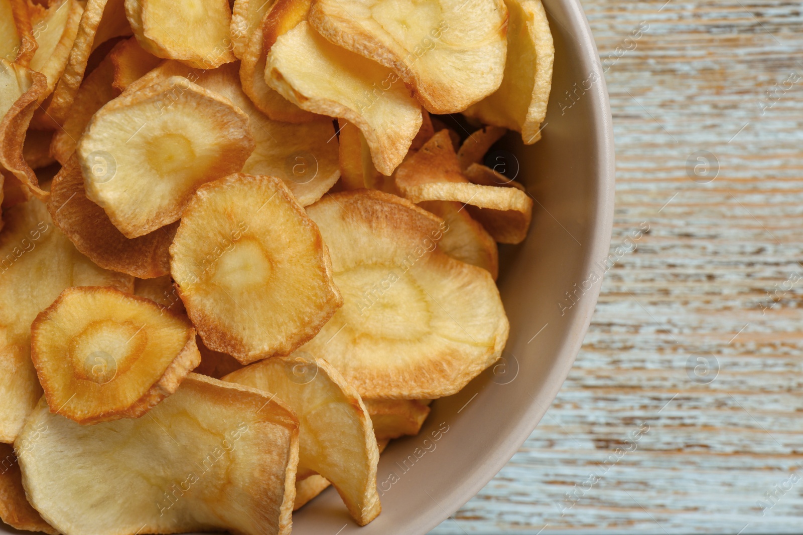 Photo of Bowl of tasty homemade parsnip chips on old light blue wooden table, top view