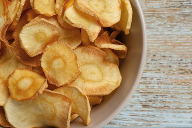 Photo of Bowl of tasty homemade parsnip chips on old light blue wooden table, top view