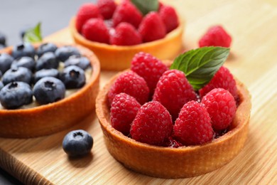 Photo of Tartlets with different fresh berries on wooden board, closeup. Delicious dessert