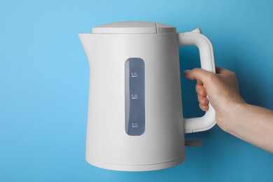 Woman holding modern electric kettle on light blue background, closeup