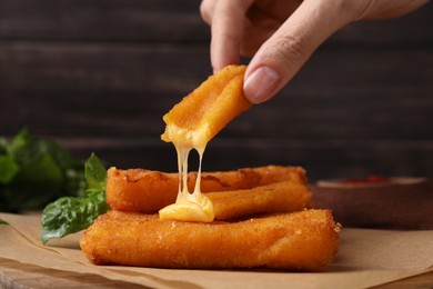 Photo of Woman taking tasty fried mozzarella stick from table, closeup