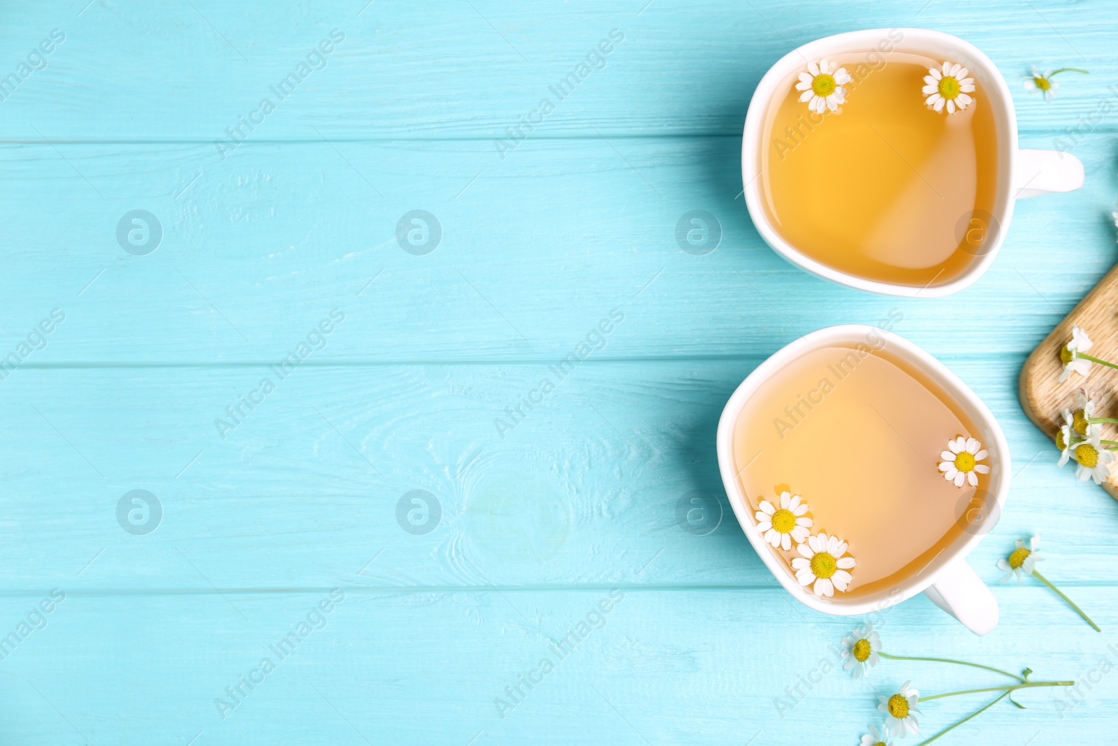 Photo of Fresh chamomile tea in cups on light blue wooden table, flat lay. Space for text