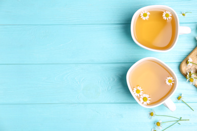 Fresh chamomile tea in cups on light blue wooden table, flat lay. Space for text