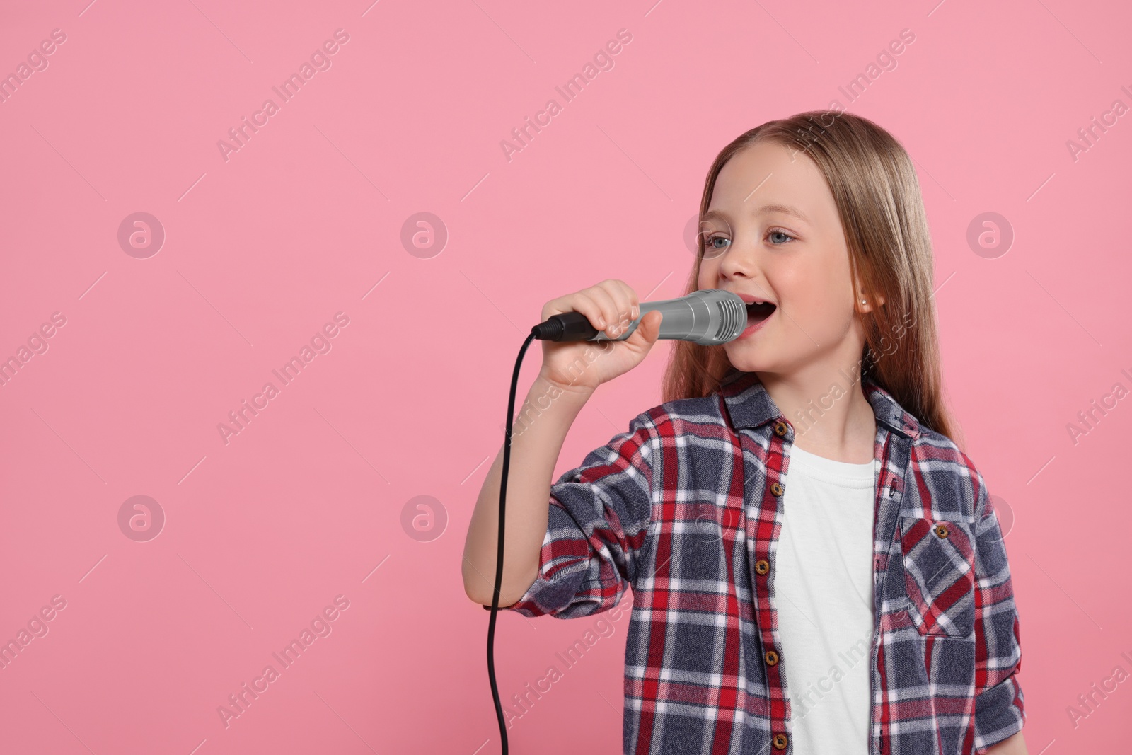 Photo of Cute little girl with microphone singing on pink background, space for text