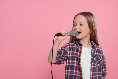 Cute little girl with microphone singing on pink background, space for text