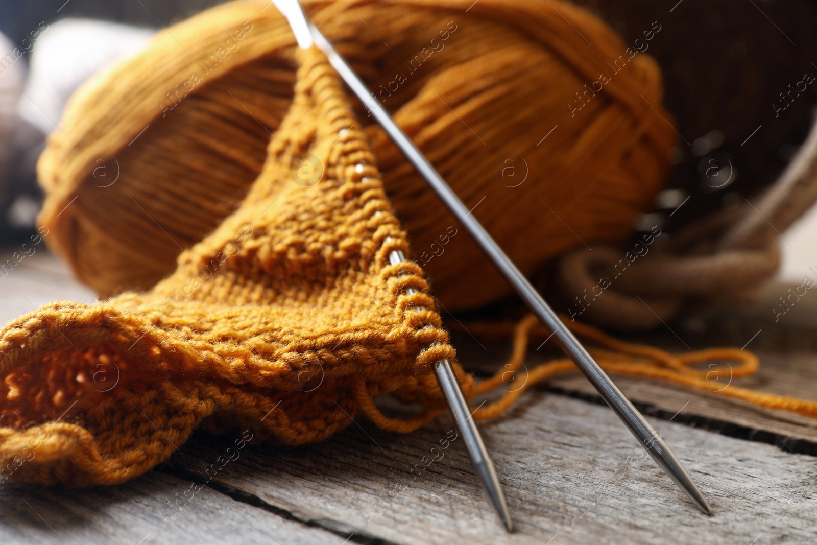 Photo of Soft orange knitting, yarn and metal needles on wooden table, closeup