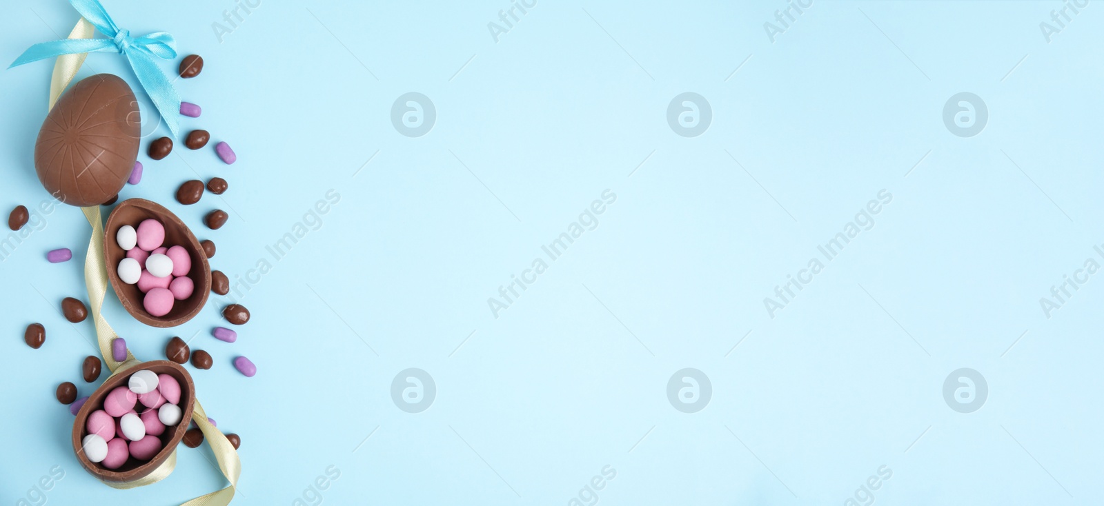 Photo of Flat lay composition with tasty chocolate eggs and candies on light blue background. Space for text