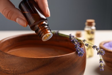 Photo of Woman dripping lavender essential oil from bottle into bowl, closeup