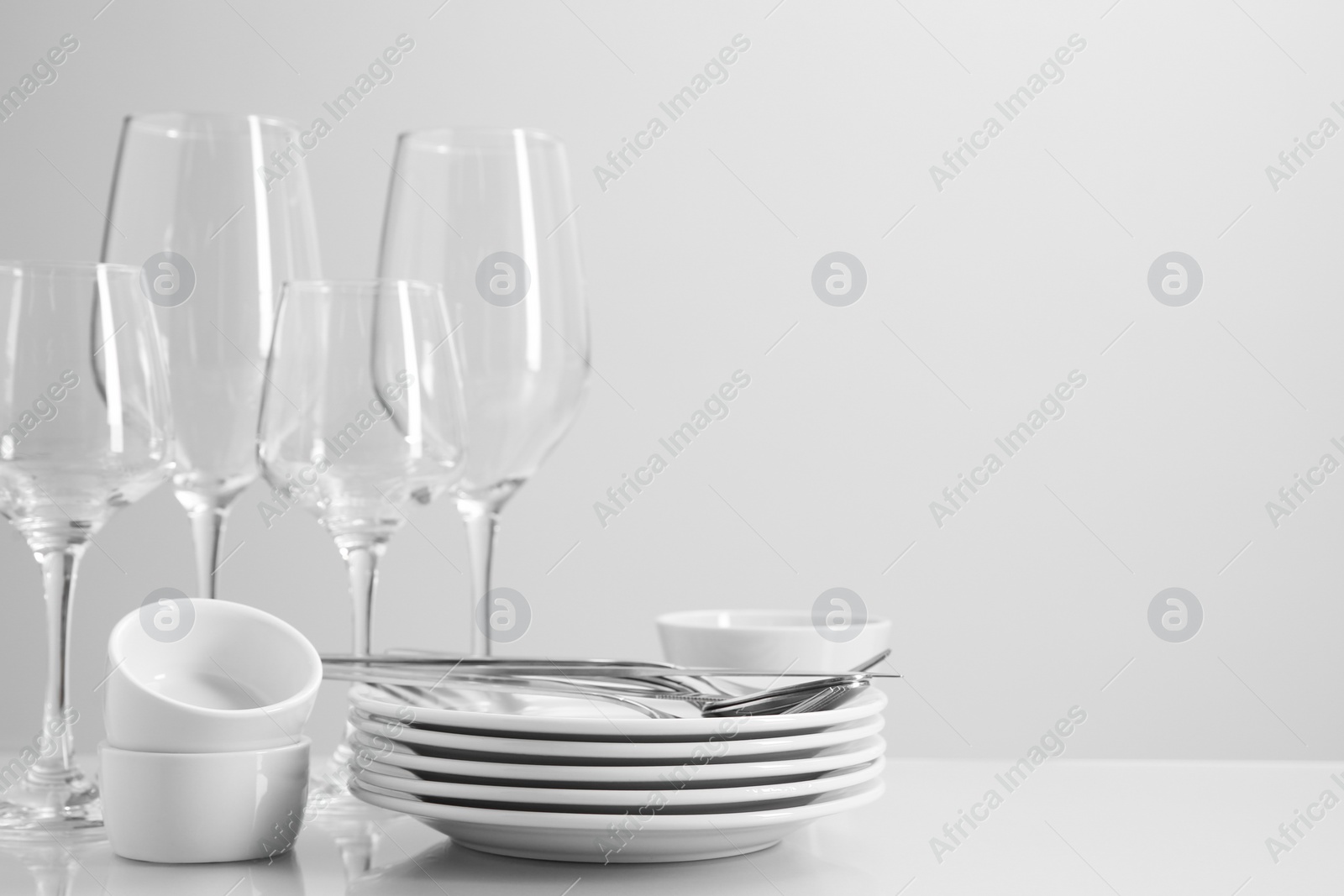 Photo of Set of many clean dishware, cutlery and glasses on light table. Space for text