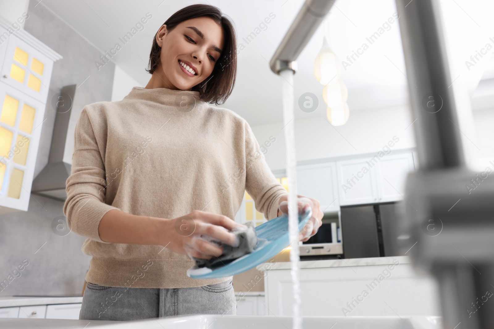 Photo of Happy woman washing plate above sink in modern kitchen, low angle view