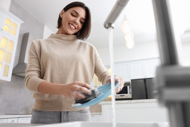 Photo of Happy woman washing plate above sink in modern kitchen, low angle view