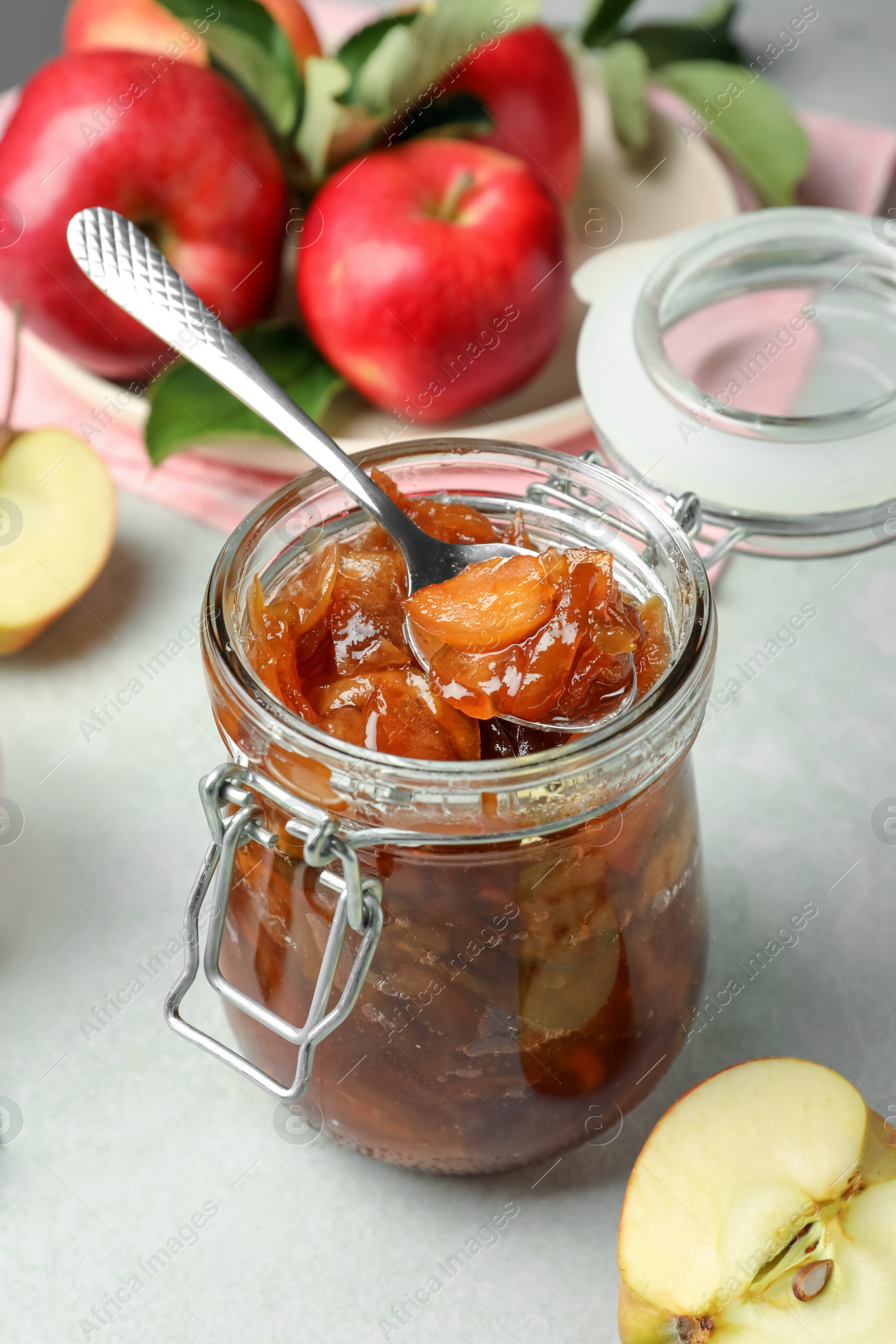 Photo of Tasty apple jam in glass jar and fresh fruits on light table