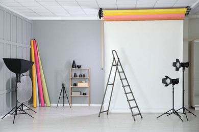 Photo of White photo background, ladder and professional lighting equipment in modern studio