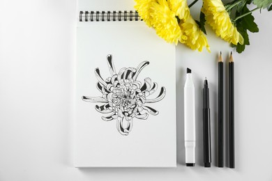 Photo of Drawing of chrysanthemum in sketchbook, flowers and art supplies on white background, flat lay