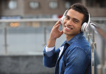 Handsome young African-American man with headphones listening to music on city street. Space for text