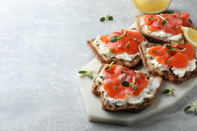 Delicious sandwiches with cream cheese, salmon and microgreens on light grey table. Space for text