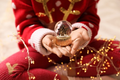 Photo of Little girl in red Christmas sweater holding snow globe, closeup