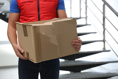 Photo of Courier with damaged cardboard box indoors, closeup. Poor quality delivery service