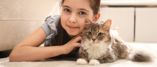 Image of Cute little girl with cat lying on carpet at home. Banner design