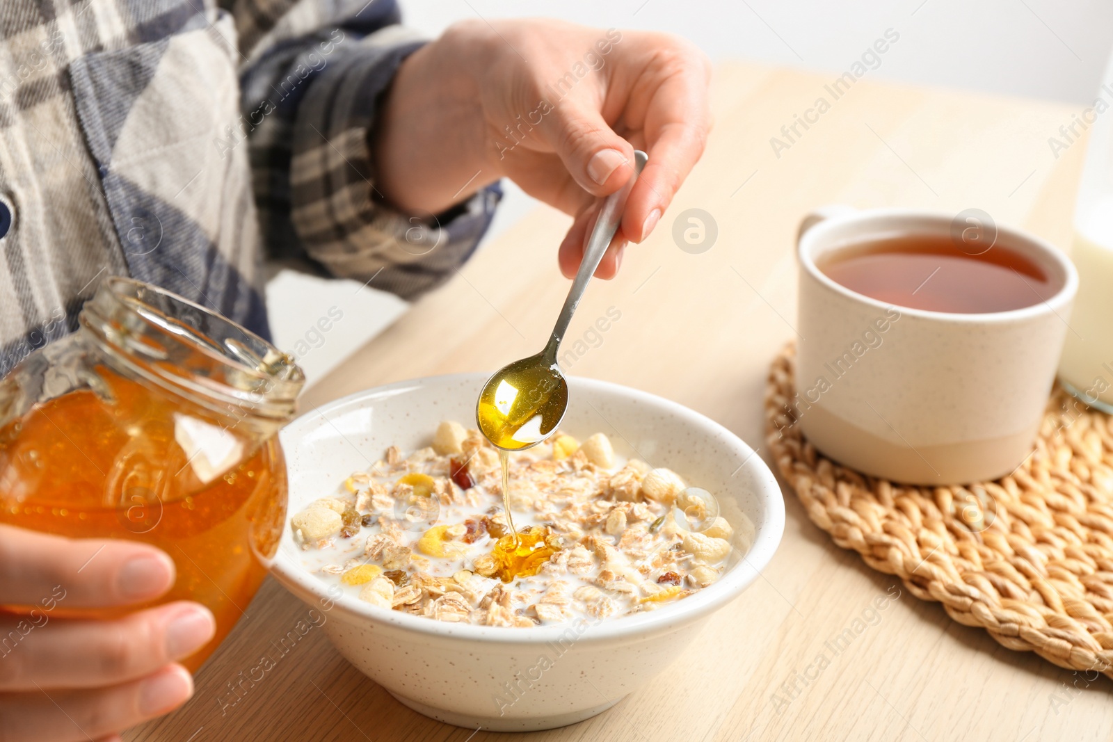 Photo of Woman putting honey into bowl with muesli at wooden table, closeup