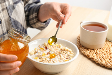 Photo of Woman putting honey into bowl with muesli at wooden table, closeup