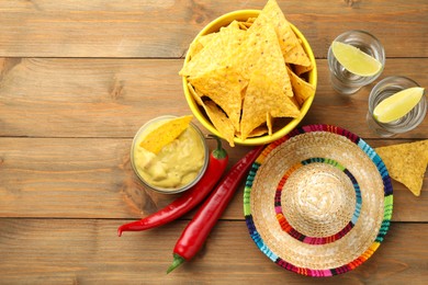 Mexican sombrero hat, tequila, chili peppers, nachos chips and guacamole on wooden table, flat lay. Space for text