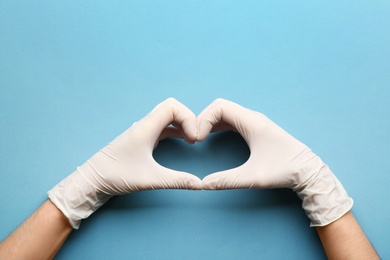 Photo of Person in medical gloves showing heart gesture against blue background, closeup of hands