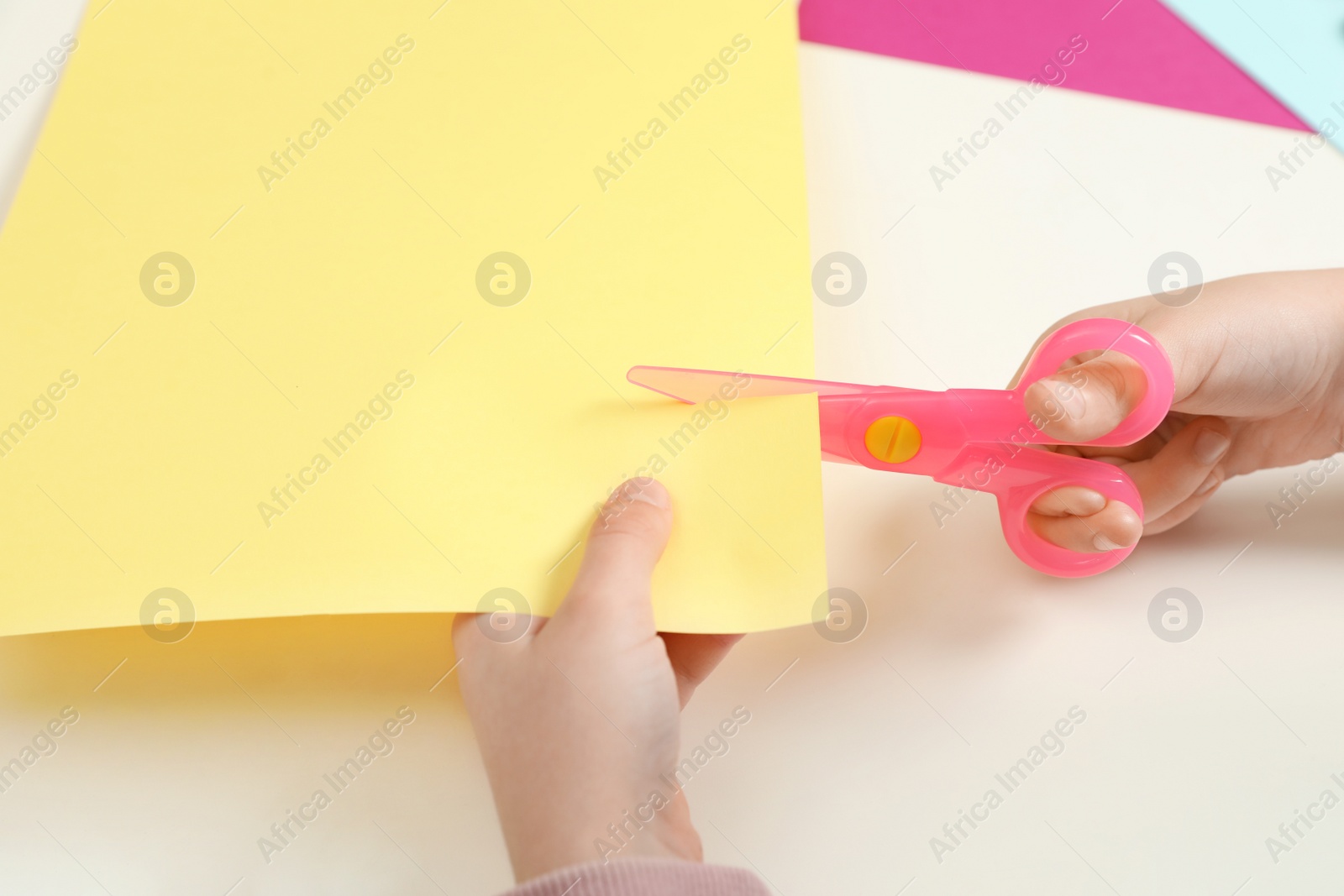 Photo of Child cutting color paper with plastic scissors at table, closeup