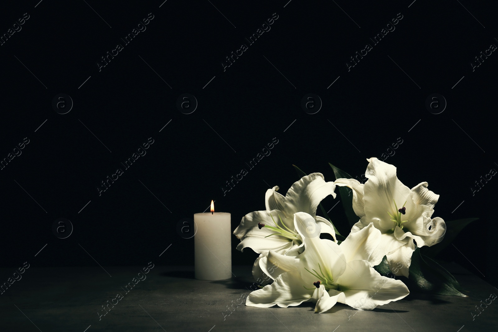 Photo of Beautiful lilies and burning candle on dark background with space for text. Funeral flowers