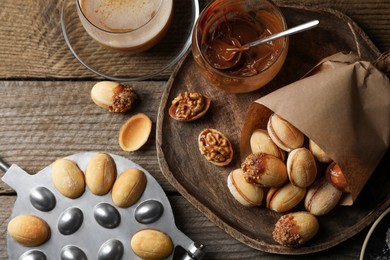 Freshly baked homemade walnut shaped cookies, boiled condensed milk, baking mold and cup of coffee on wooden table, flat lay