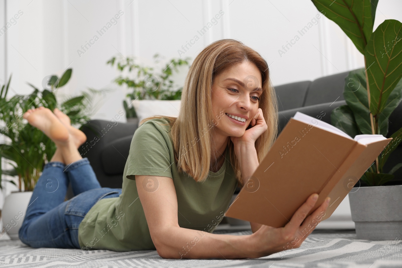 Photo of Woman reading book on floor in room with beautiful houseplants