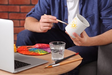 Photo of Man learning to decorate cup while watching online course indoors, closeup. Time for hobby