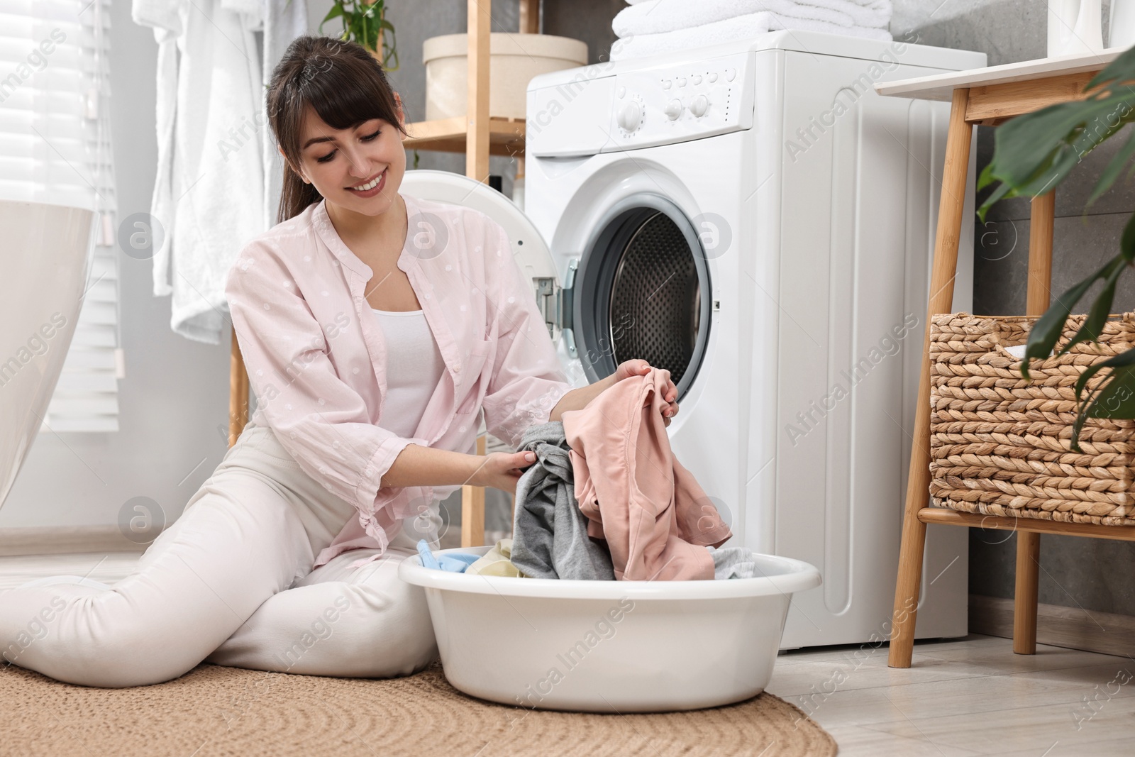 Photo of Happy young housewife with laundry near washing machine at home