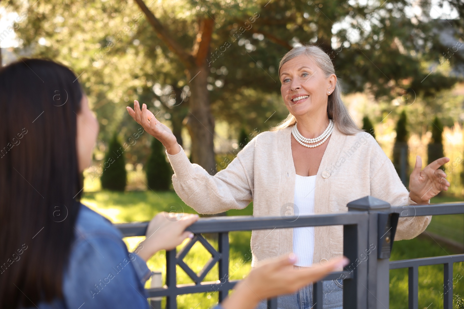 Photo of Friendly relationship with neighbours. Happy women talking near fence outdoors