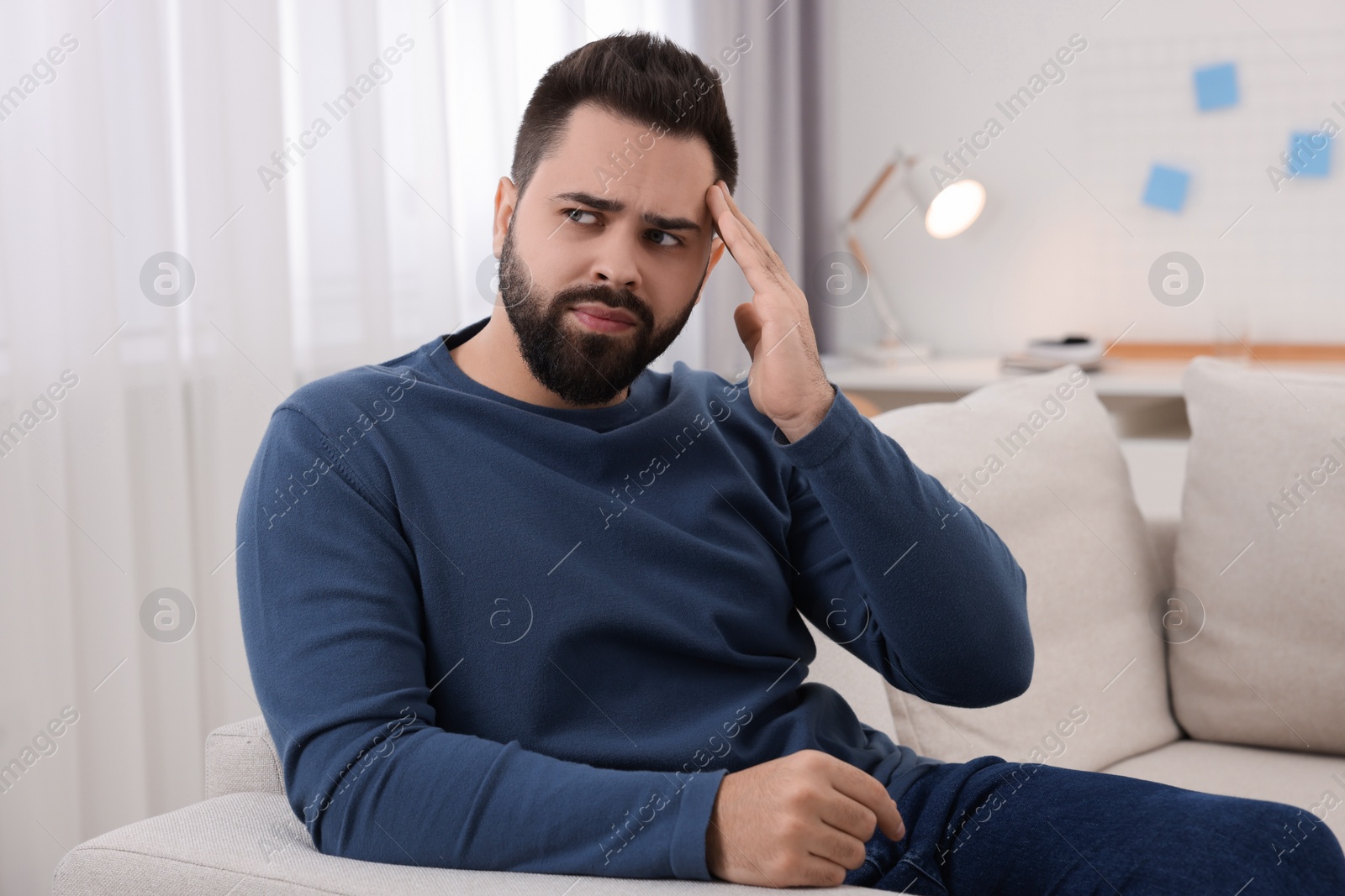 Photo of Man suffering from headache on sofa at home