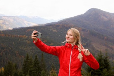 Happy young woman taking selfie with phone in mountains