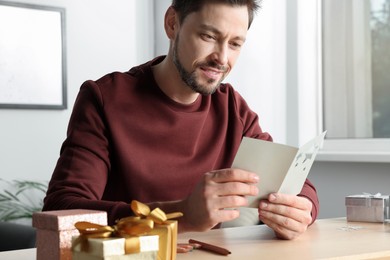 Happy man reading greeting card at wooden table in room