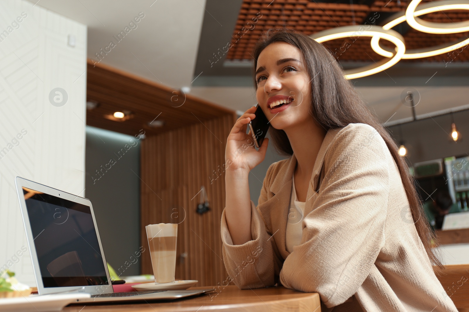 Photo of Young blogger with laptop talking on phone in cafe